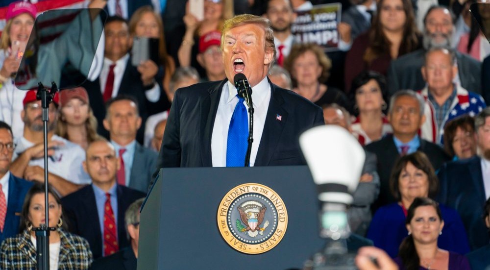 President Trump speaks animatedly in front of a large crowd.